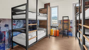 A dormitory room with bunk beds, wooden flooring, and a view of a cityscape through an open door.