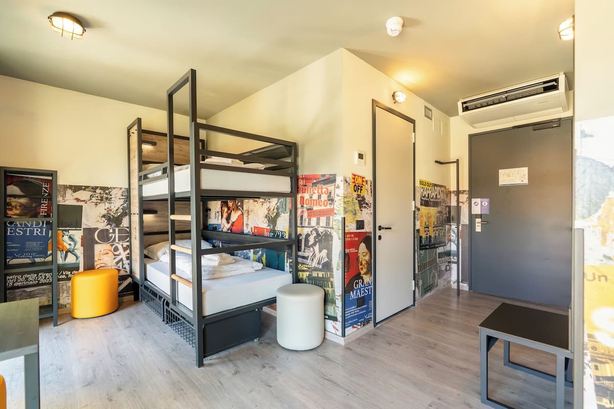 A room with a bunk bed, a small table, a trash bin, and a door with an air conditioning unit above it.