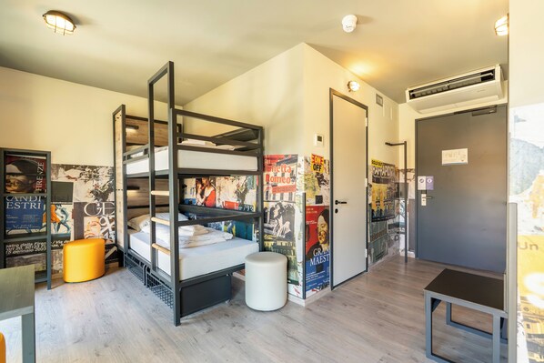 A room with a bunk bed, a small table, a trash bin, and a door with an air conditioning unit above it. - a&o Hostel Firenze Campo Di Marte (Florence)