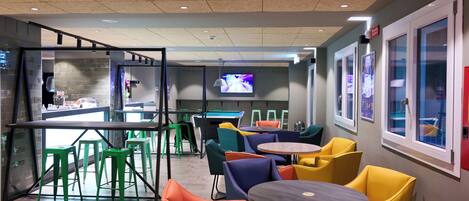 A modern indoor space with a bar area, multiple seating options including chairs and tables, and a television screen.