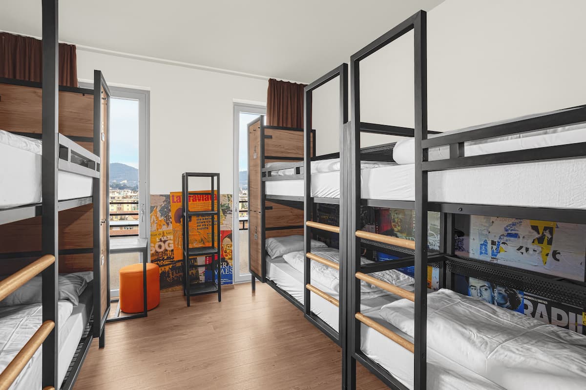 A dormitory room with bunk beds, a wooden floor, and a poster on the wall.