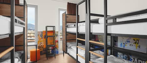 A dormitory room with bunk beds, a wooden floor, and a poster on the wall.