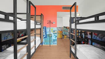 A dormitory room with bunk beds, a wooden floor, and a colorful mural on the wall.