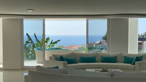 En moderne stue med en hvid hjørnesofa, store gulv til loft vinduer og havudsigt.