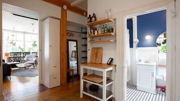 A room with a wooden floor, white walls, and a kitchen area with white cabinets and shelves.