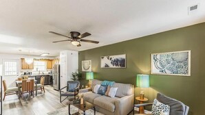 A living room with a sofa, coffee table, and lamps. There is a dining area with chairs and a table. The room has a ceiling fan. - Greenleaf Comfort Retreat 4 Beds Decatur (Decatur)