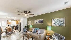 A living room with a sofa, coffee table, and lamps. There is a dining area with chairs and a table. The room has a ceiling fan. - Greenleaf Comfort Retreat 4 Beds Decatur (Decatur)