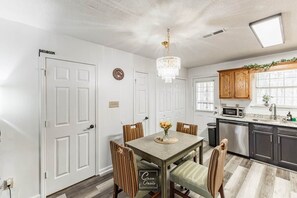 A dining area with a table, chairs, a chandelier, and a kitchen with cabinets and a microwave. - Greenleaf Comfort Retreat 4 Beds Decatur (Decatur)