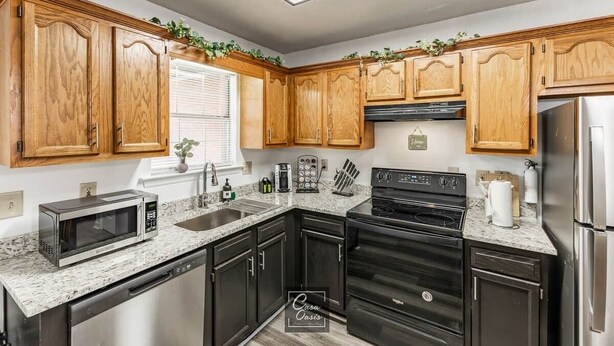 A kitchen with wooden cabinets, a stainless steel refrigerator, a microwave, and a dishwasher. - Greenleaf Comfort Retreat 4 Beds Decatur (Decatur)