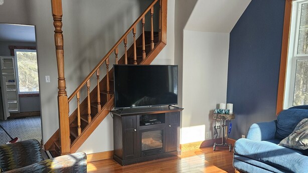 A spacious living room with a wooden staircase, a flat-screen TV, and a blue sofa.