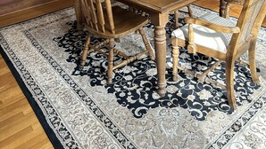 Ein Esszimmer mit Holztisch und -stühlen, einem gemusterten Teppich und einem Hirschgeweih an der Wand.