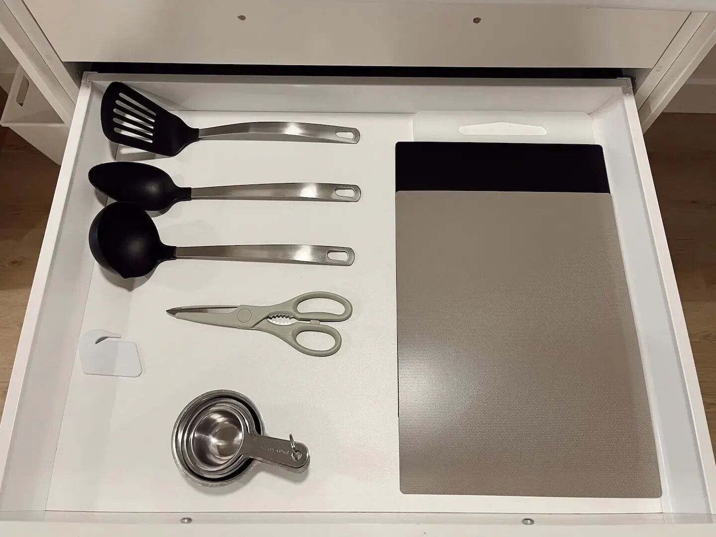 Cajón con utensilios de cocina, como espátula, cuchara, tijeras y taza medidora.