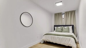 Ein Schlafzimmer mit einem Bett, einem runden Spiegel und einem Fenster mit Vorhängen.