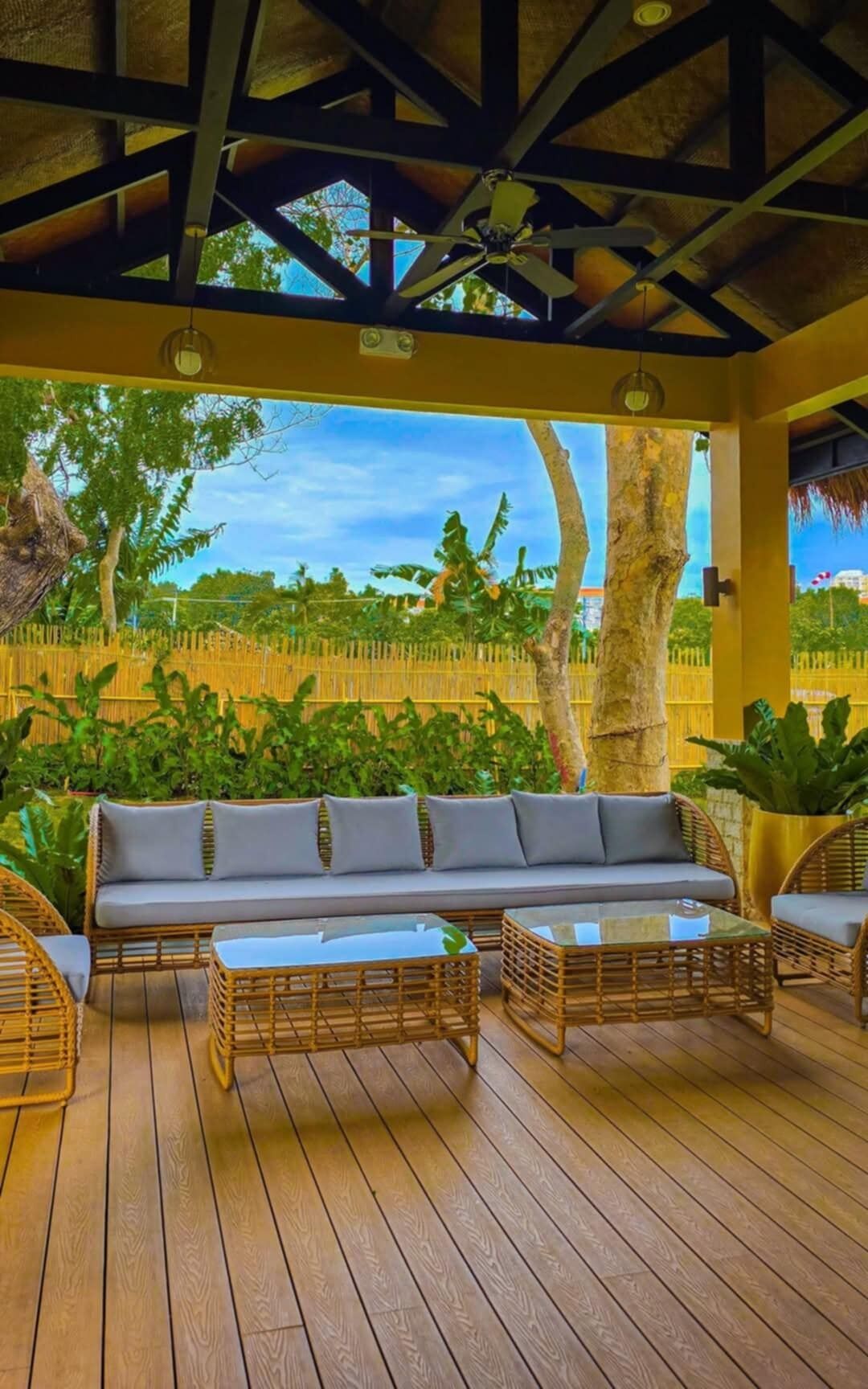 A covered outdoor seating area with a wooden deck, a sofa, and wicker chairs.