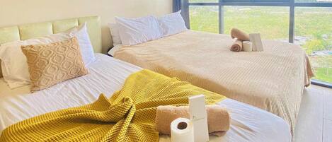 A hotel room with two beds, a large window with a city view, an air conditioning unit, and a yellow blanket on one bed.