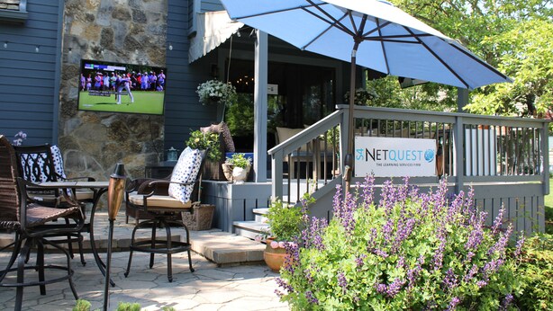 An outdoor seating area with patio furniture, a stone wall, and a sign for NetQuest. - Awesome home 17th hole for the Memorial Tournament! Great for corporate outing. (Dublin)