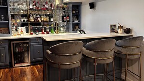 A bar area with a marble backsplash, multiple liquor bottles, and three bar stools. - Awesome home 17th hole for the Memorial Tournament! Great for corporate outing. (Dublin)