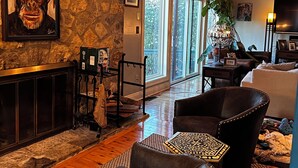 A cozy living room with a stone wall, a fireplace, leather chairs, and a large window with a view of greenery. - Awesome home 17th hole for the Memorial Tournament! Great for corporate outing. (Dublin)