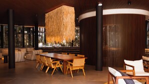 A spacious indoor area with a large wooden dining table surrounded by chairs, a hanging light fixture, and a view of greenery through large windows. - Luxury Penthouse Miraluna 324 (Tulum)