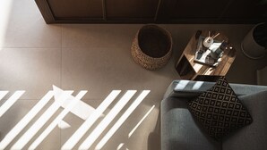 A modern living room with a grey sofa, a woven basket, and a small wooden side table with a tray holding a candle and decorative items. - Copal Experience The Port (Chania)