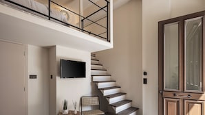 A modern interior with a staircase, a flat-screen TV, a wooden door, and a seating area. - Copal Experience The Port (Chania)