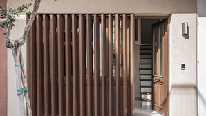 A modern building entrance with a wooden slat gate, a staircase leading inside, and a small outdoor seating area. - Copal Experience The Port (Chania)