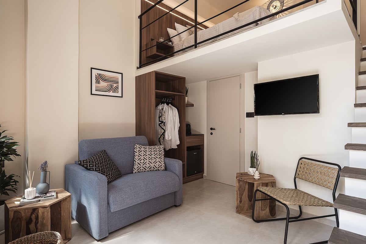 A modern living room with a grey sofa, a wooden coffee table, a wicker chair, and a TV mounted on the wall.