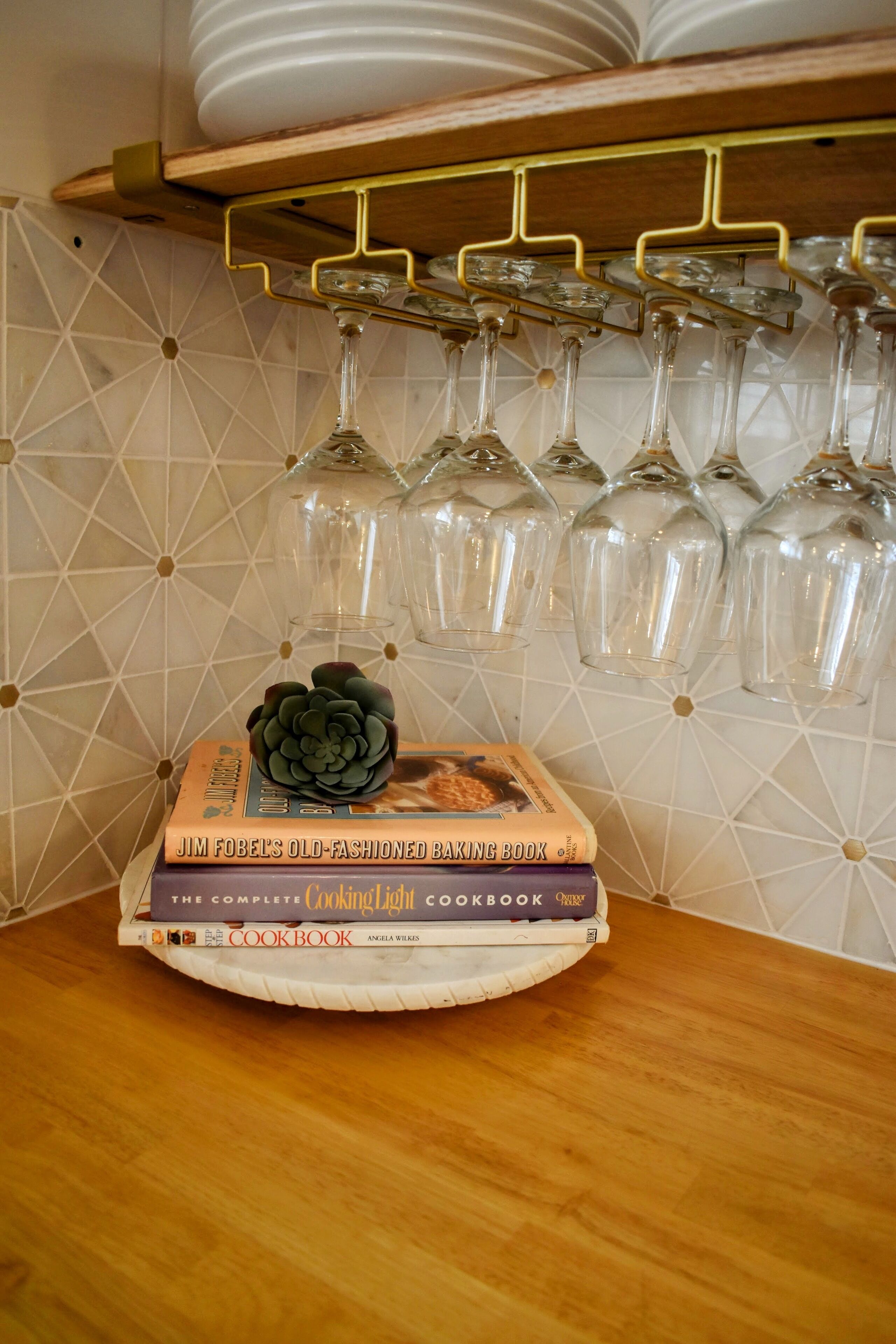 A kitchen counter with a stack of cookbooks, a succulent plant, and a wine rack with glasses.