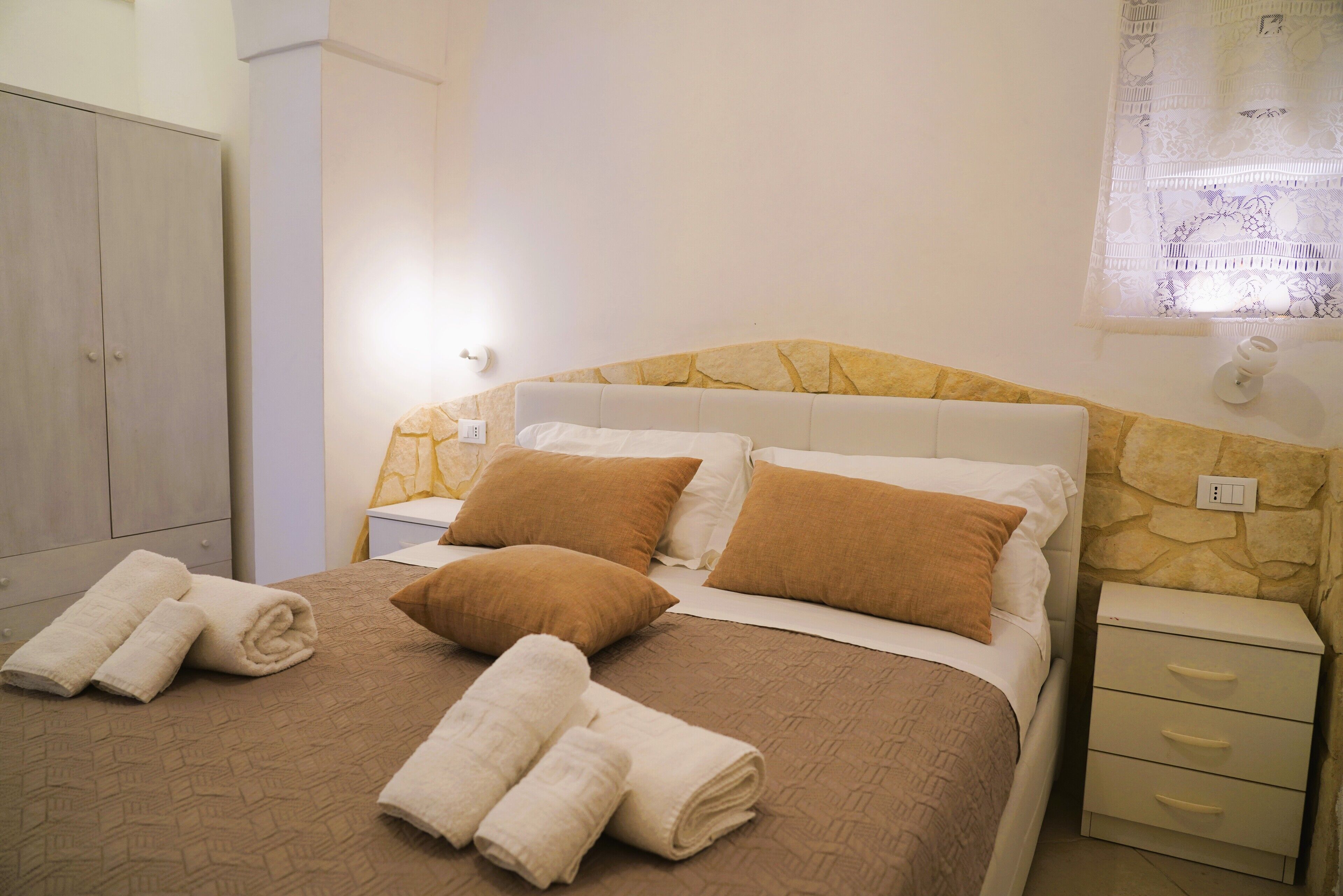 Una cama bien hecha con ropa de cama marrón y blanca, dos almohadas marrones y un juego de toallas sobre la cama.