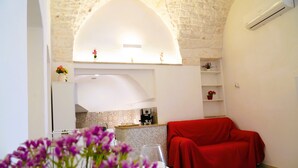 A modern kitchen with a stone wall, a red covered sofa, and a vase of flowers on the counter. - La Casetta in Pietra - Arcuève (Ostuni)