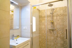 A modern bathroom with a glass-enclosed shower, a white sink with two bottles, and patterned tiles. - La Casetta in Pietra - Arcuève (Ostuni)