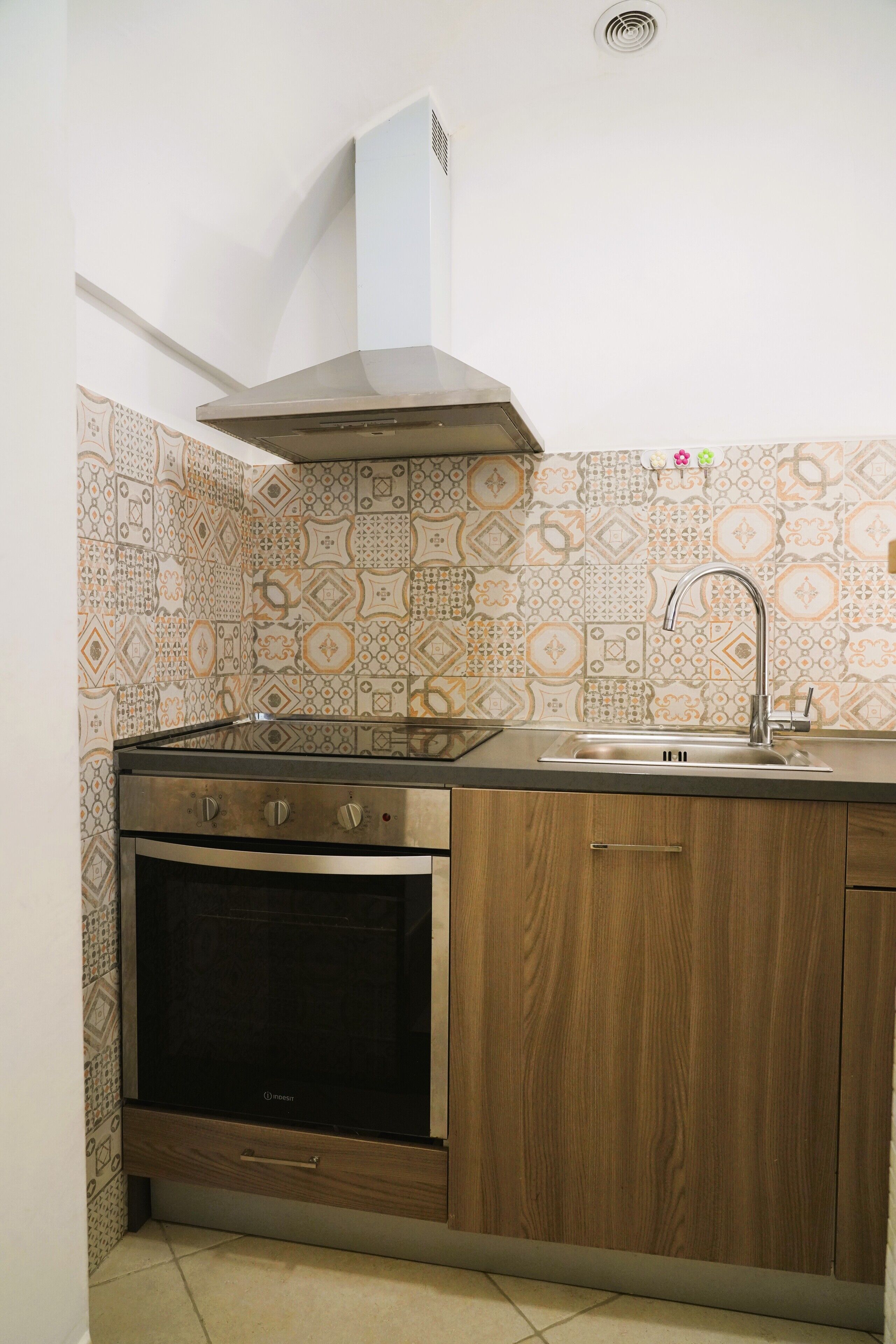 A kitchen with a built-in oven, a stainless steel range hood, a sink, and wooden cabinets.