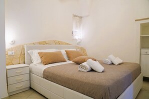 A neatly made bed with a brown bedspread, two pillows, and rolled towels on the side. - La Casetta in Pietra - Arcuève (Ostuni)