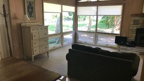 Een kamer met een houten eettafel, een zwarte bank, een witte ladekast en een televisie.
