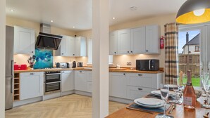 A modern kitchen with white cabinets, stainless steel appliances, and a wooden dining table set for a meal.