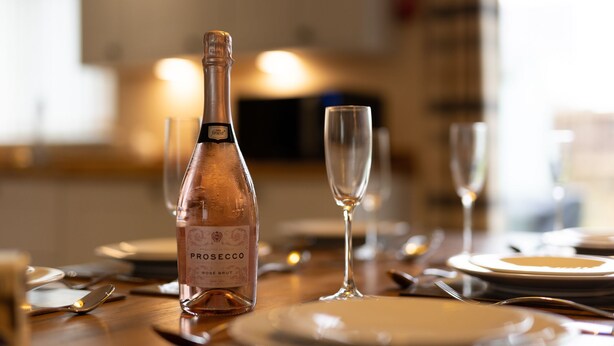 A bottle of prosecco and two glasses on a dining table.