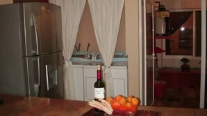 Una cocina con refrigerador, estufa y lavaplatos. Hay una botella de vino y un cuenco de fruta en la encimera.