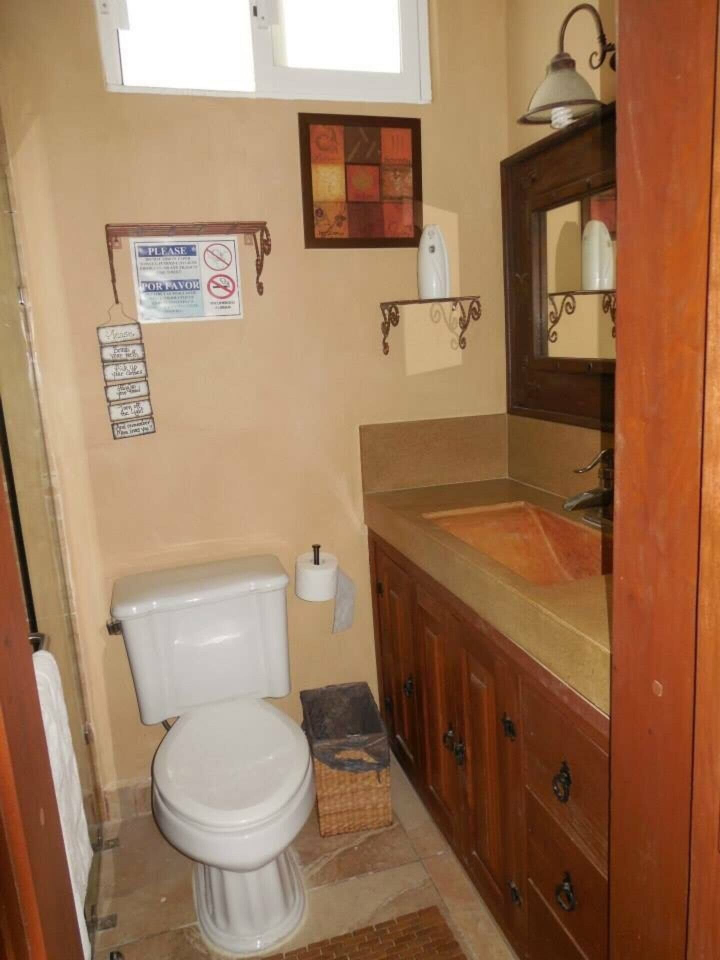 Une petite salle de bain comprenant des toilettes, un lavabo et un miroir. Un panneau est accroché au mur et un objet décoratif est placé au-dessus des toilettes.