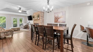 A spacious dining area with a wooden table and chairs, a chandelier, and a stone accent wall.