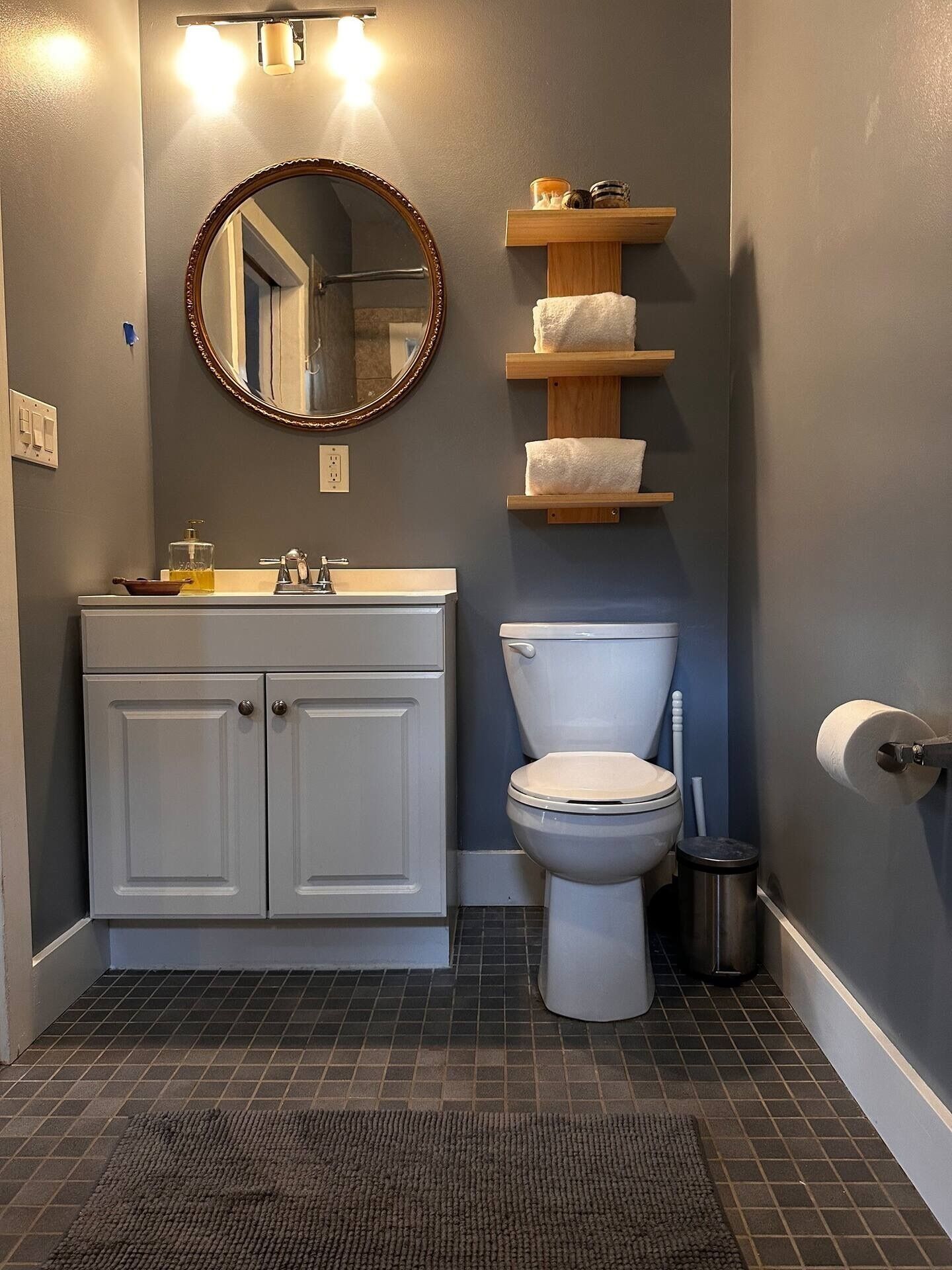 Un baño con inodoro blanco, lavabo con espejo y estantes de madera con toallas.