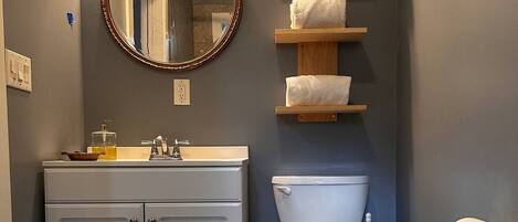 Un baño con inodoro blanco, lavabo con espejo y estantes de madera con toallas.