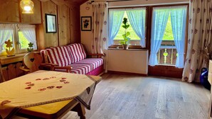 Une pièce chaleureuse avec un plafond en bois, un canapé à rayures, une table recouverte d’une nappe à motifs en forme de cœur et des fenêtres avec des rideaux.