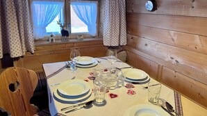 L’intérieur d’un chalet en bois, avec une table à manger dressée pour quatre personnes, une fenêtre avec des rideaux et un crâne de cerf servant de décoration au mur.