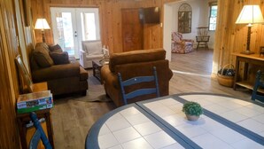 Una sala de estar acogedora con paredes de madera, un sofá, una silla, un televisor y una mesa de comedor con una planta.