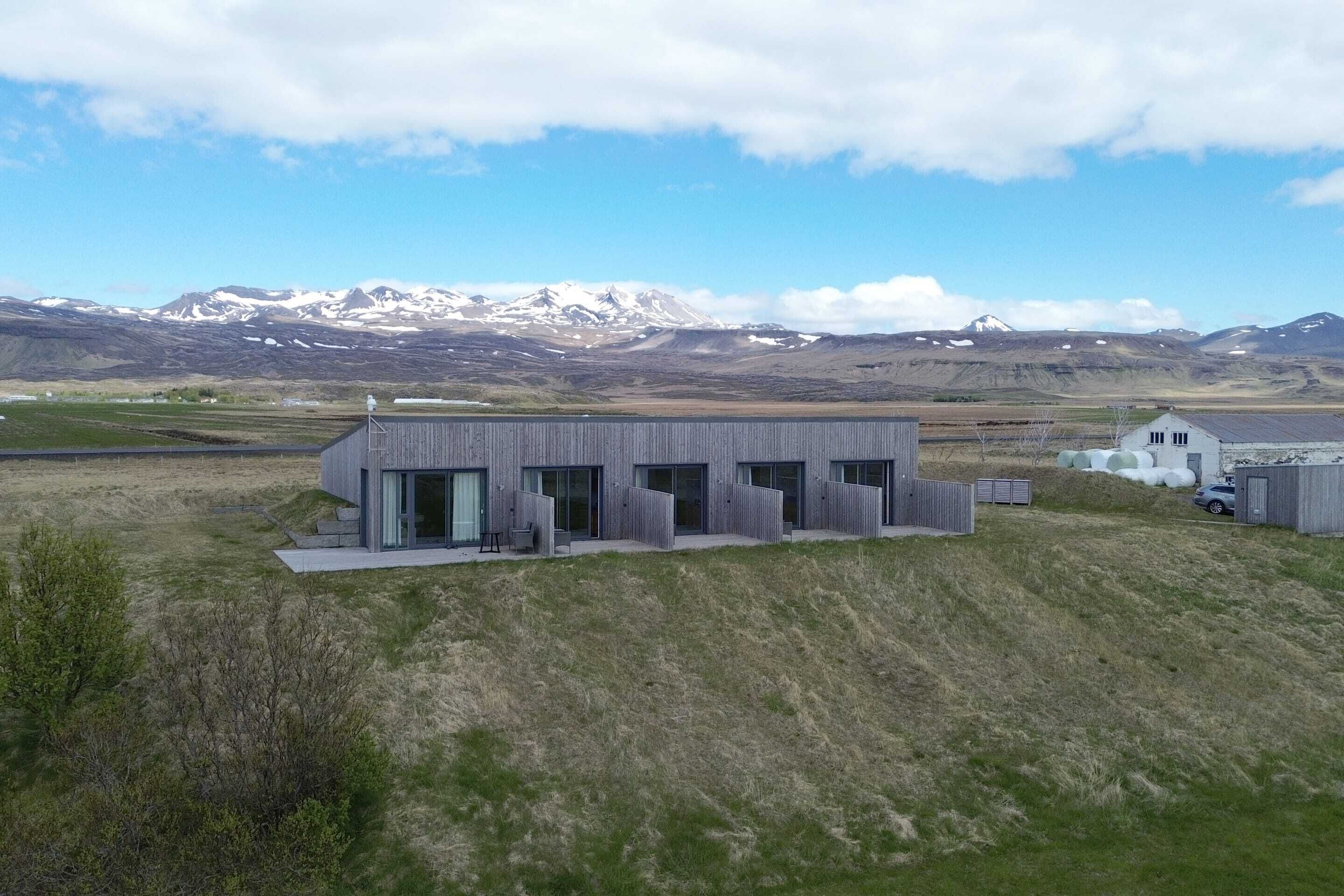 A modern building with large windows and a flat roof, surrounded by a grassy landscape and mountains in the background.