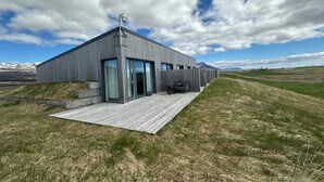 A modern building with a flat roof, large windows, and a wooden deck. - Eiðhús Apartments (Eyja- og Miklaholtshreppur)