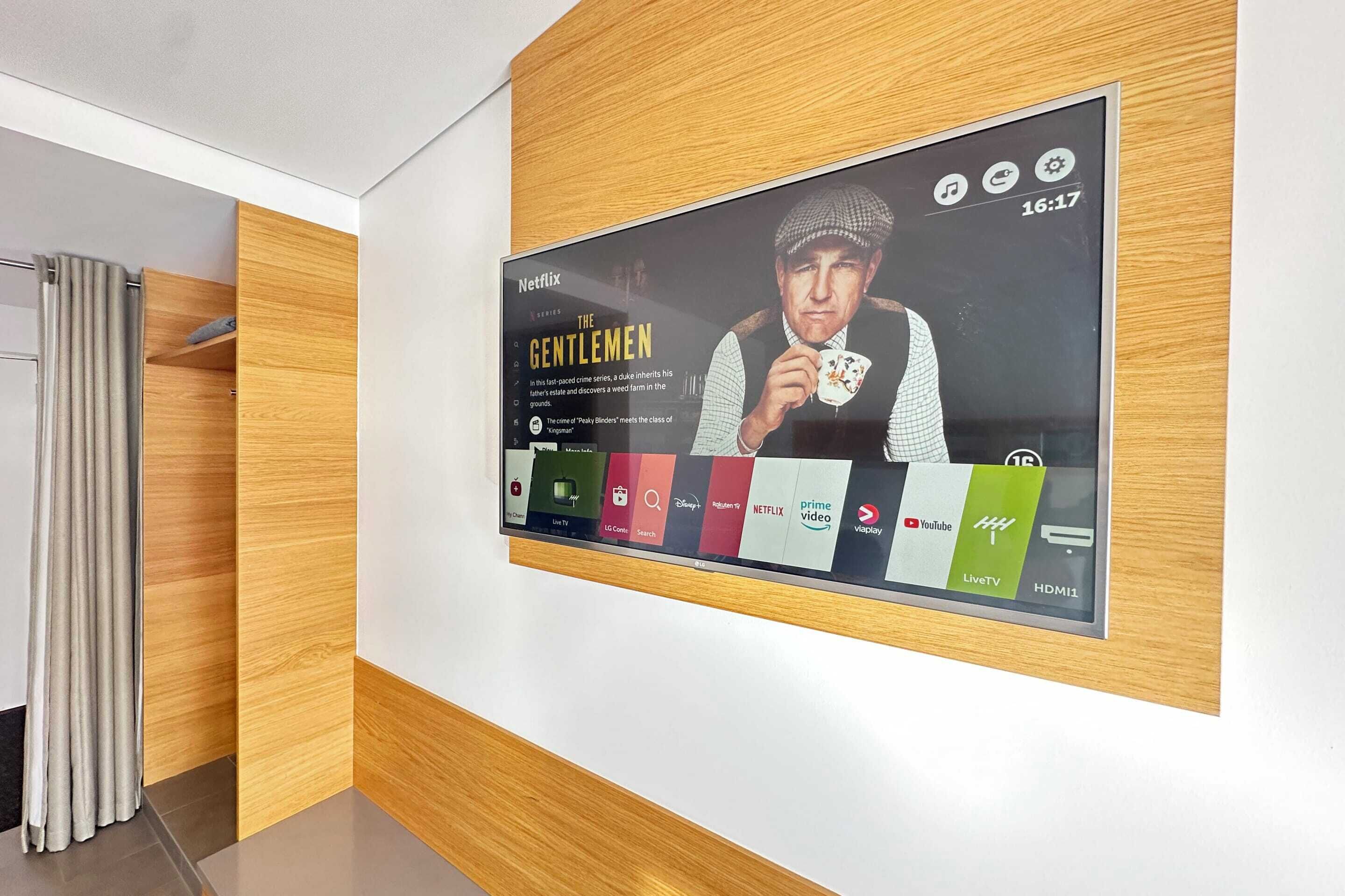 A digital display advertising 'The Gentlemen' on Netflix, with a wooden panel wall and a curtain on the left.
