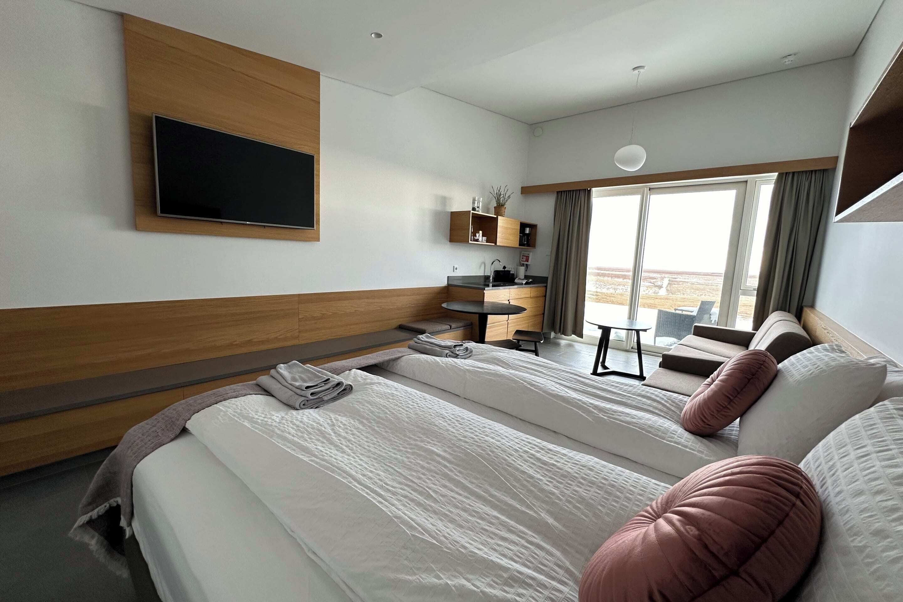 Una habitación de hotel moderna con una cama grande, un televisor de pantalla plana montado en la pared, un escritorio pequeño con una silla y un ventanal con vistas.