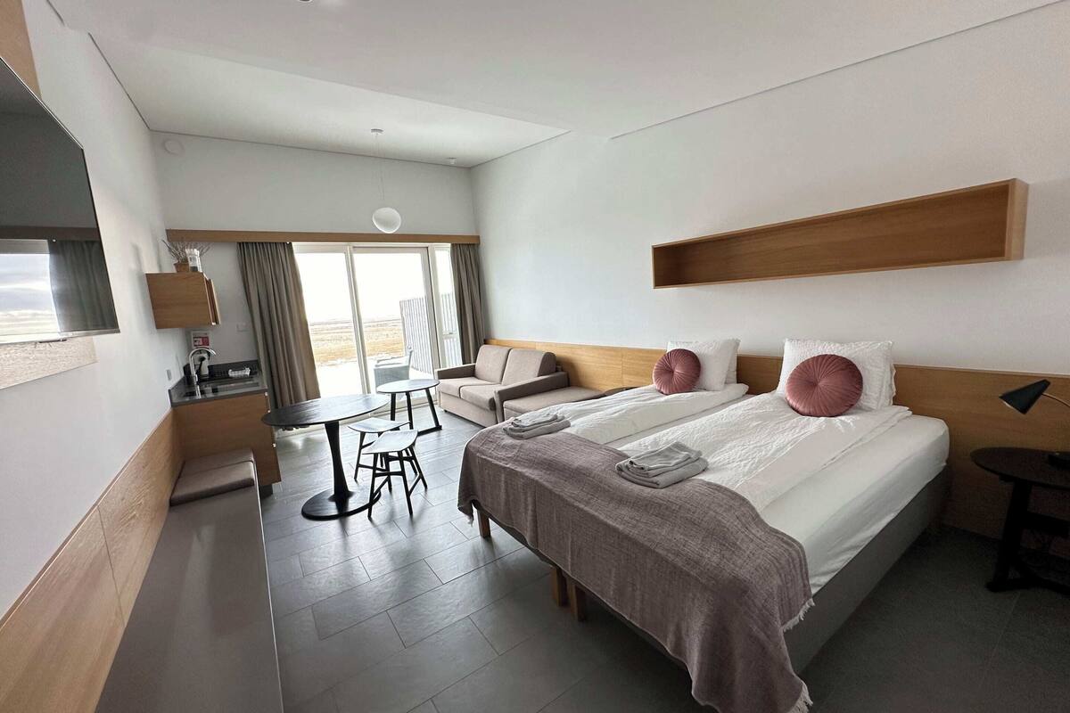 A modern hotel room with a large bed, a sofa, a dining table, and a TV.