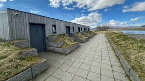 A modern building with a grey facade and a paved walkway leading to a door. - Eiðhús Apartments (Eyja- og Miklaholtshreppur)